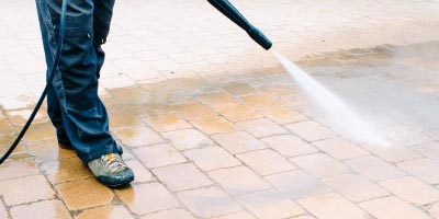 Person power washing a brick patio